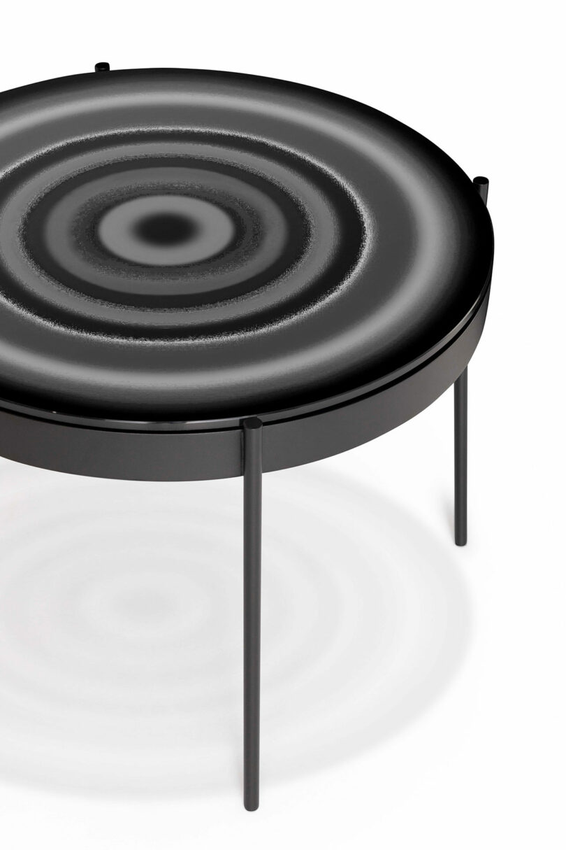 A round black table with a concentric circle pattern on the tabletop. It has four slender black legs.